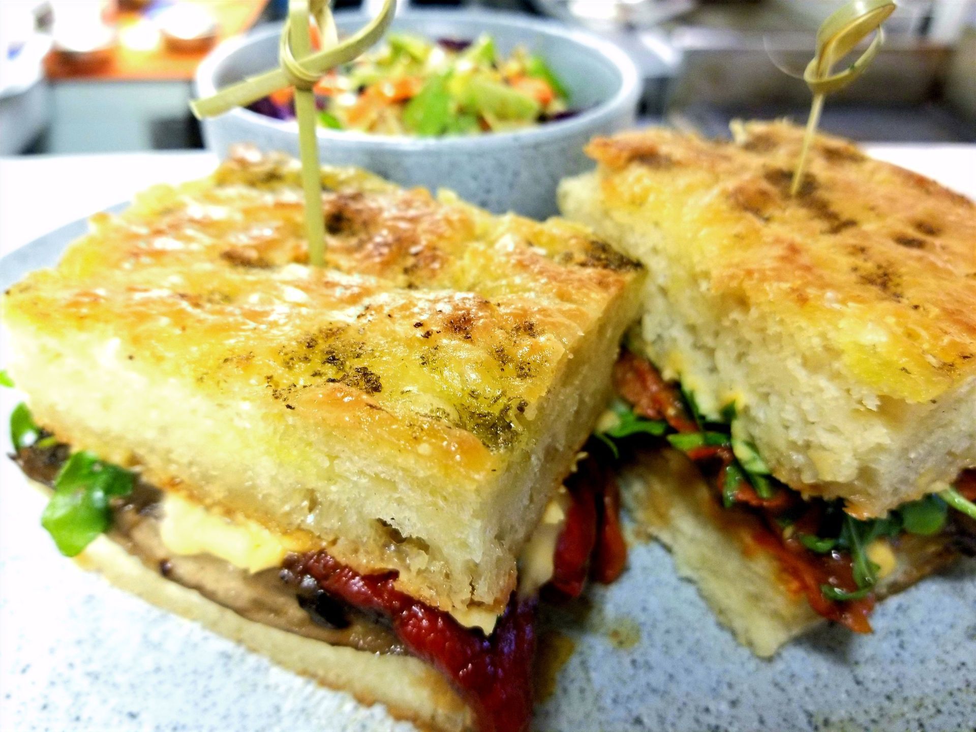 A close up of a sandwich on a plate with a salad in the background.