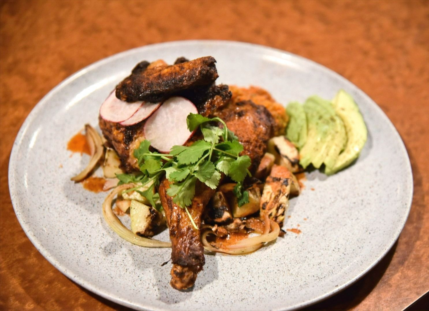 A plate of food with meat, vegetables and avocado on a table.