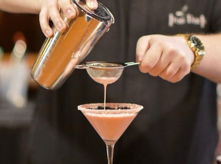 A bartender is pouring a drink into a martini glass