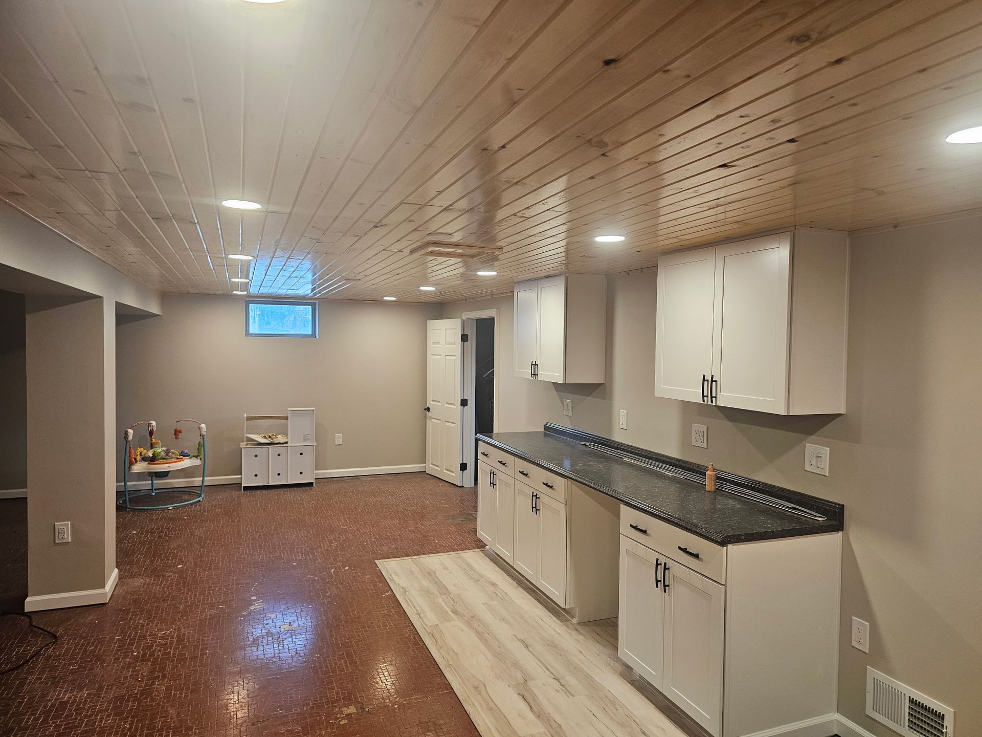 Basement with white cabinets, dark countertop, wood ceiling, and laminate flooring.