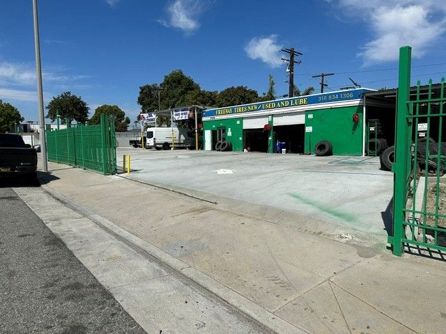 Green auto repair shop with open bay and fenced driveway under a blue sky