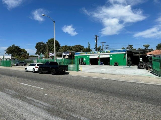 Bright green auto shop with parked pickup trucks along a sunny street under a blue sky.