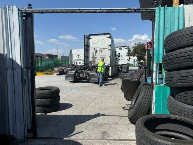 Truck yard entrance with a worker in a high-visibility vest near a white trailer and stacked tires