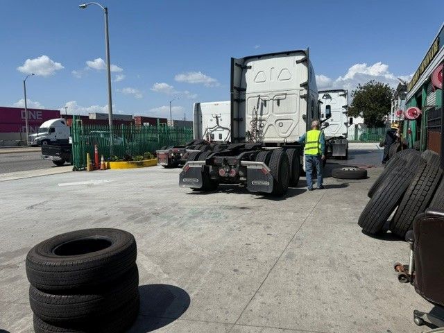 Truck chassis in a tire yard with a worker in a high-visibility vest and stacked tires nearby