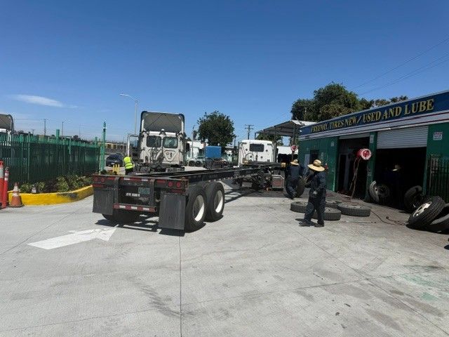 Tow truck parked in a paved lot beside a building, with a worker standing nearby under a clear blue sky.