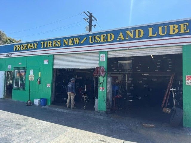 Auto repair shop storefront with green facade and open garage bays labeled “Freeway Tires New/Used and Lube.”