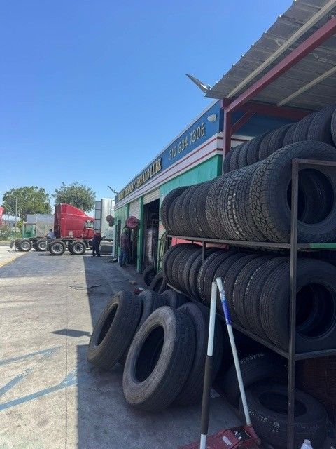Outdoor tire shop with stacks of used tires, leaning tools, and a red vehicle under the awning