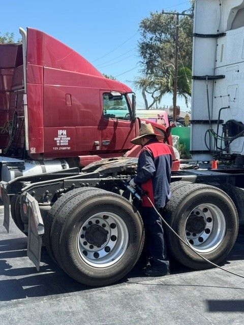 Red semi-truck with driver outside, parked beside a white tanker trailer in a lot.