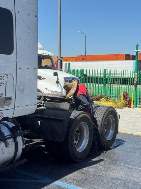 Truck driver working on a white semi-truck beside a green fence on a sunny day