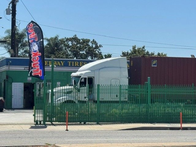 White semi-truck behind green fence at a roadside business with a red cargo trailer