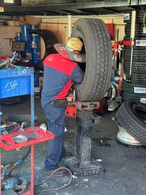 Mechanic working on a large tire in an auto repair shop, using a tire mounting machine.