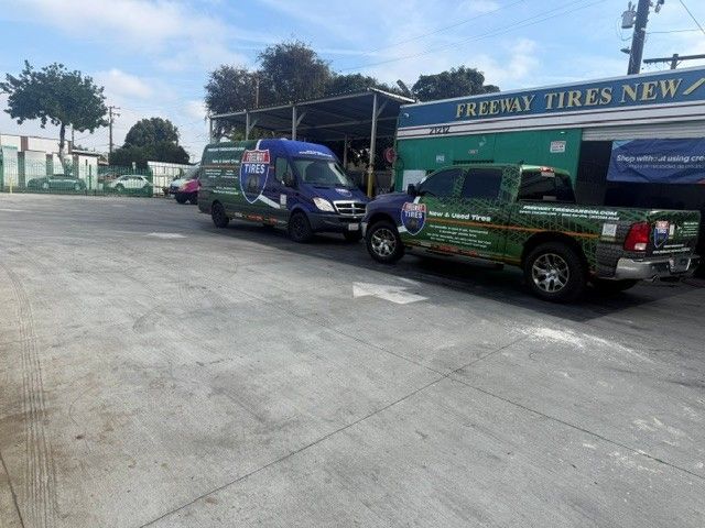 Two service trucks parked outside a tire shop with a green sign and open garage bays.