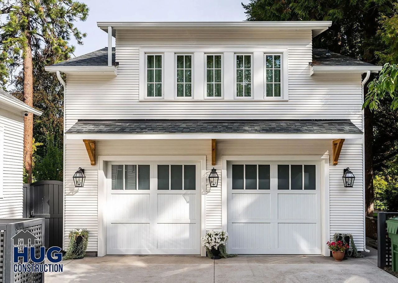 A white house with two white garage doors and a black roof.