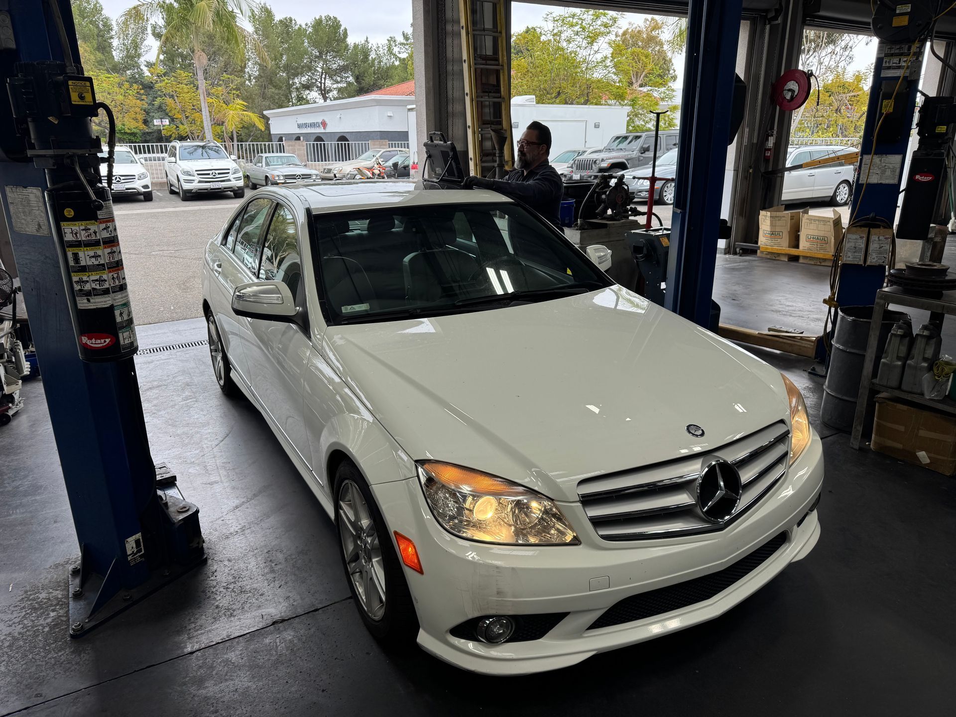 White Mercedes sedan at an auto service bay with its hood open near a lift