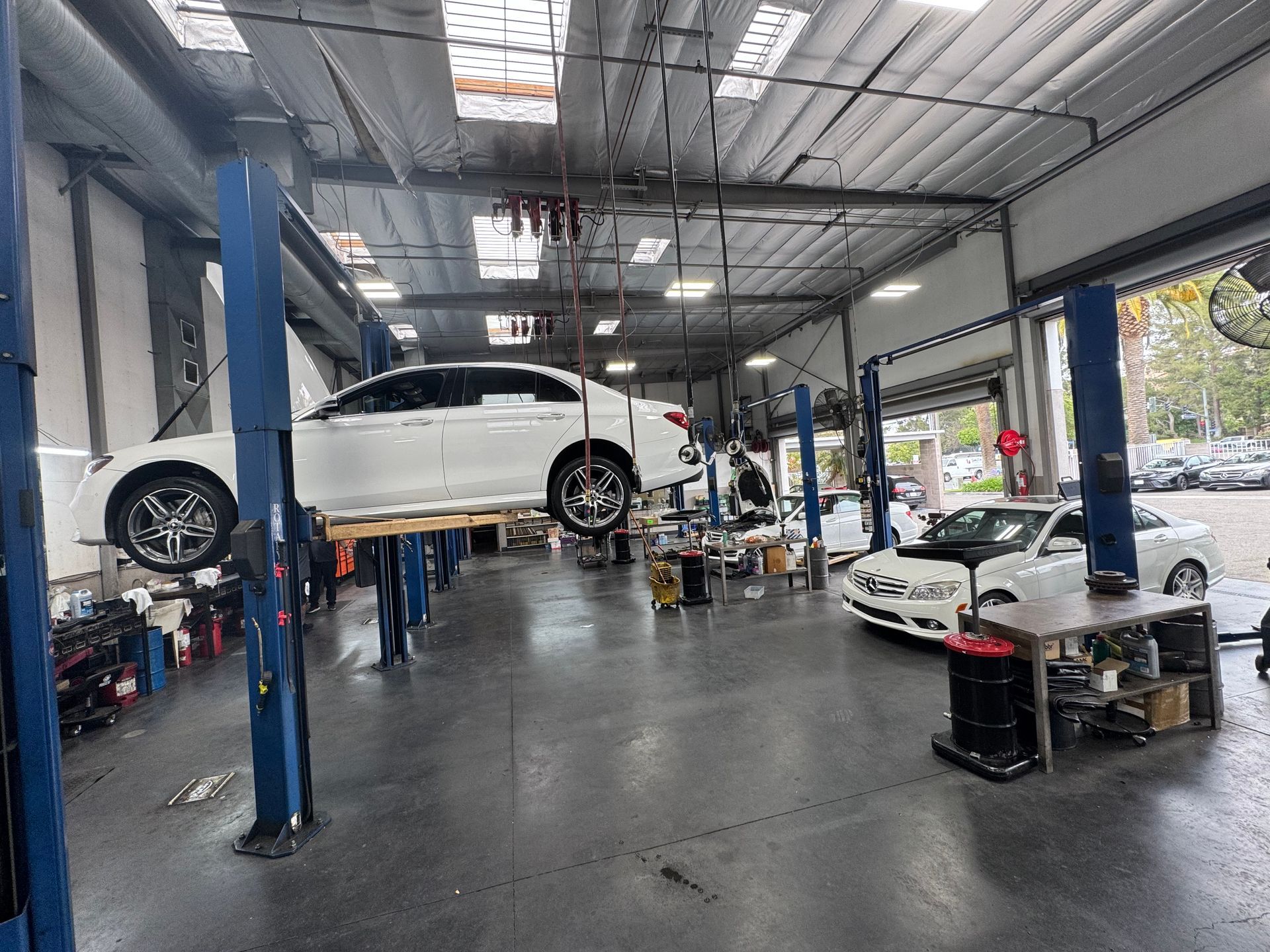 Car repair shop with a white car lifted on a hoist and another white car parked inside.