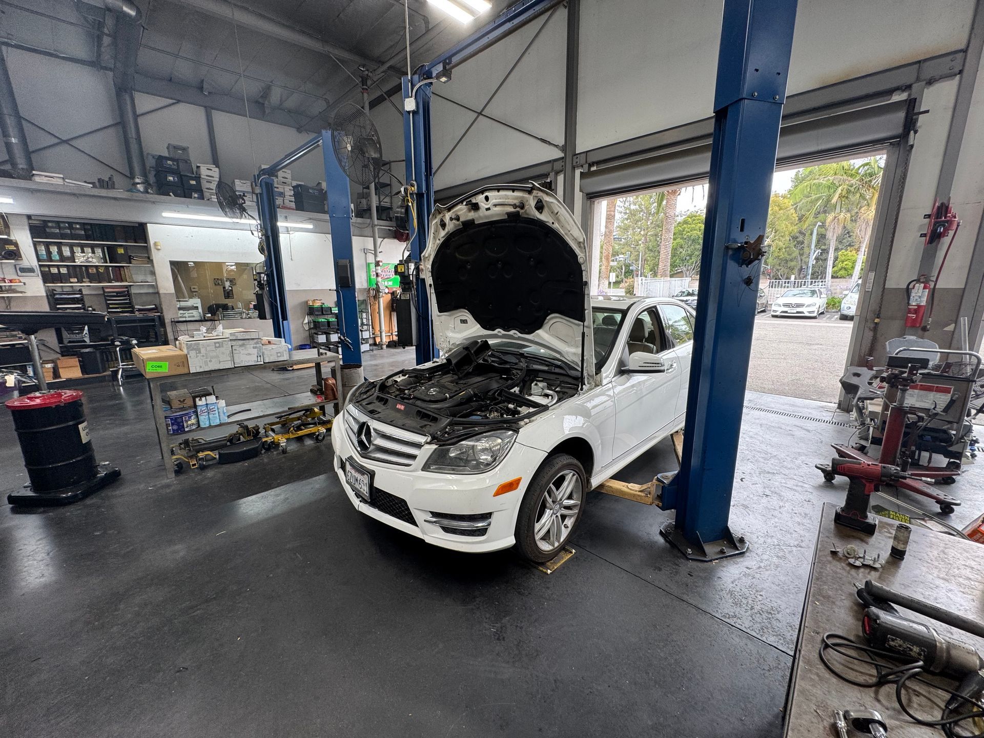 White car with hood open in an auto repair shop with blue lifts and tools around it