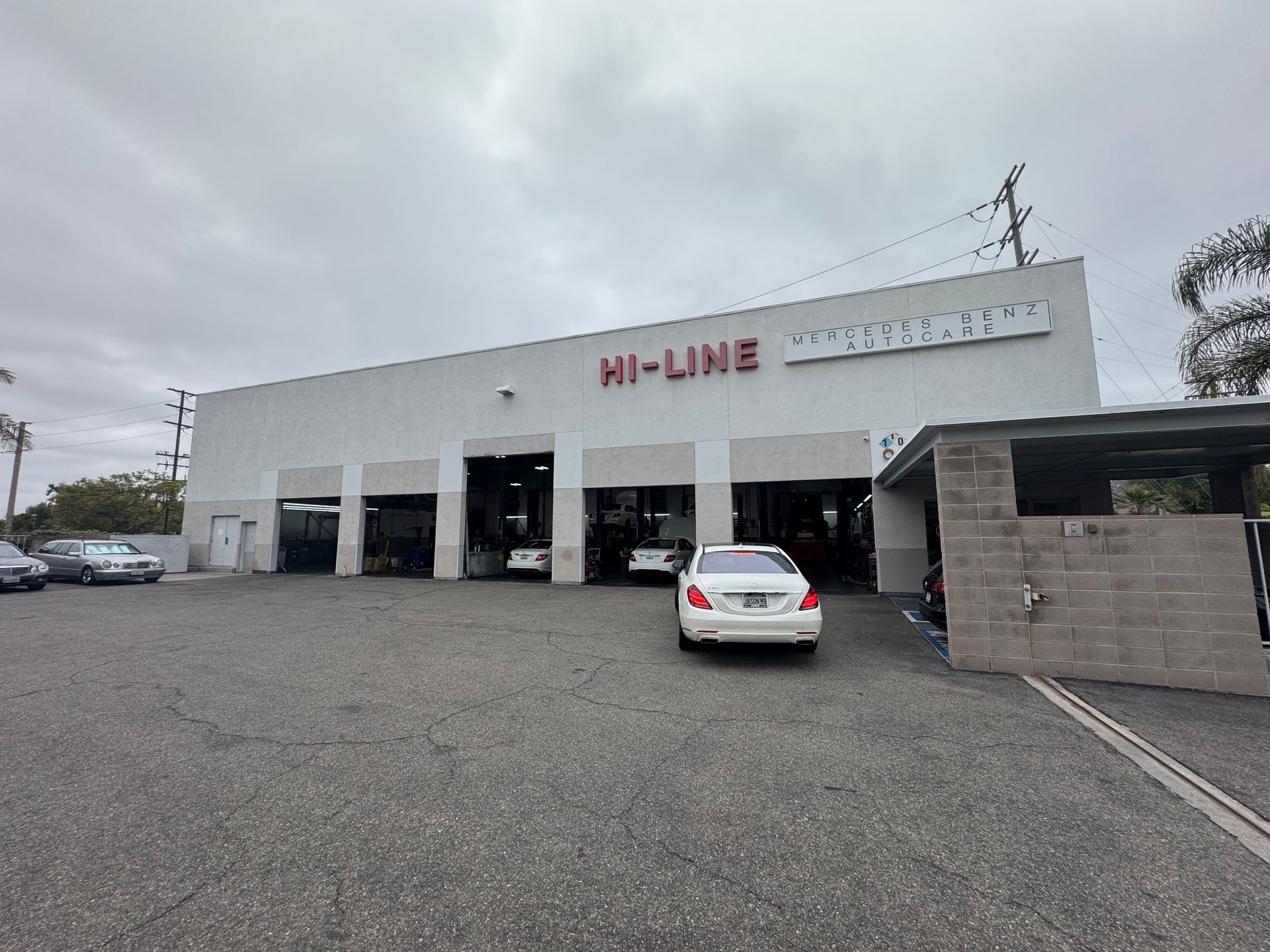 Auto repair shop exterior with large white building, open garage bays, and a parked silver car