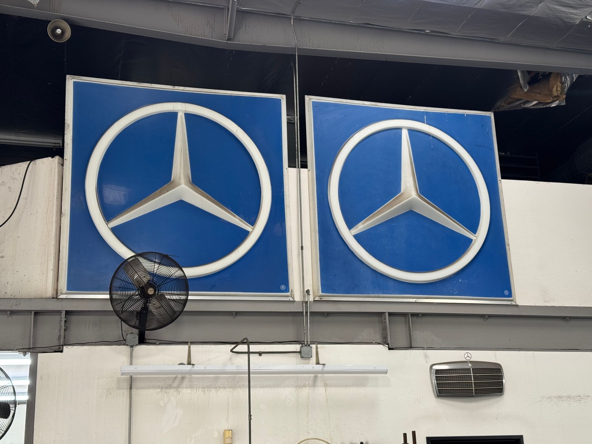 Two blue Mercedes-Benz logos mounted above a wall inside a garage-like space