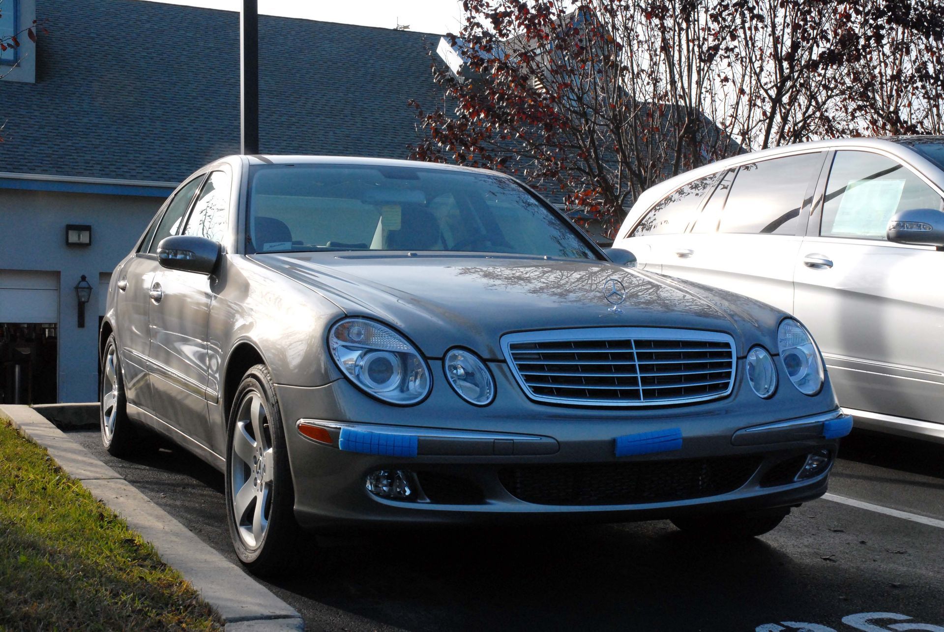 Silver Mercedes-Benz sedan parked in a driveway beside a white car outside a house