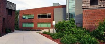 A large brick building with a lot of windows is surrounded by trees and bushes.