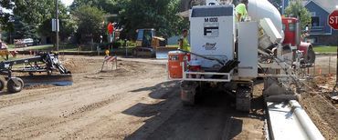A concrete mixer is pouring concrete on a dirt road.