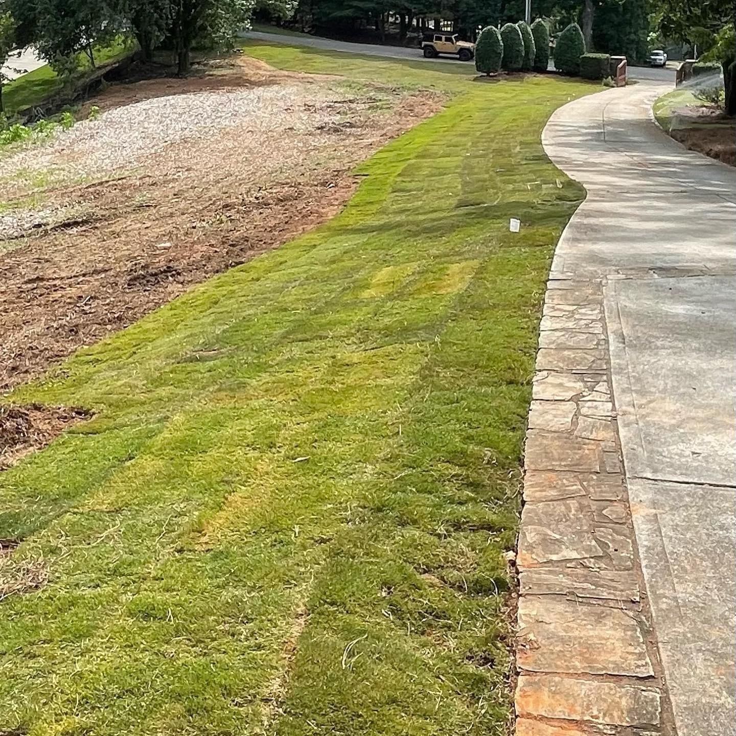 Green lawn next to a concrete driveway and a dirt hillside.