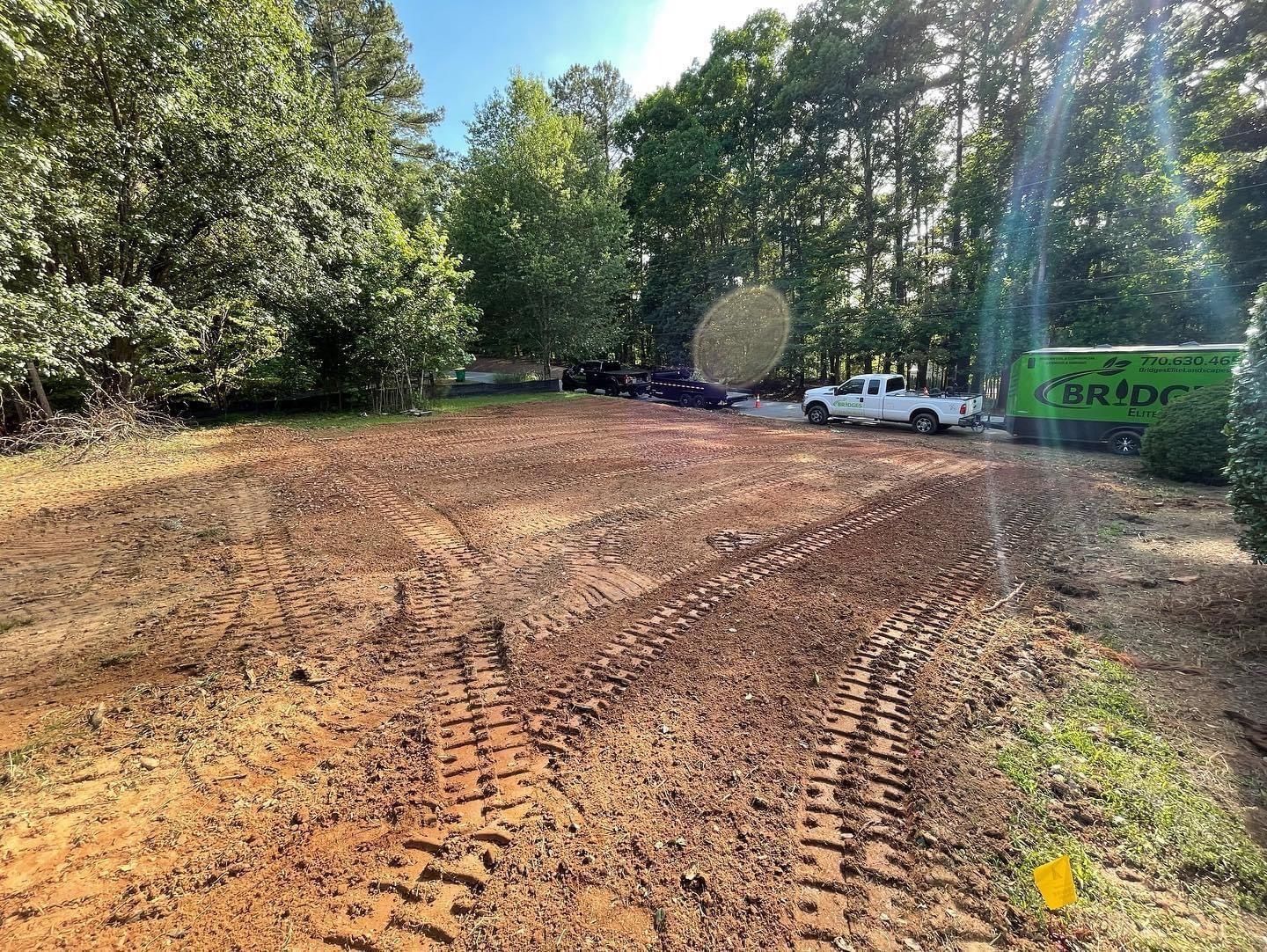 Cleared, muddy lot with tire tracks, trees in background, and a white truck.