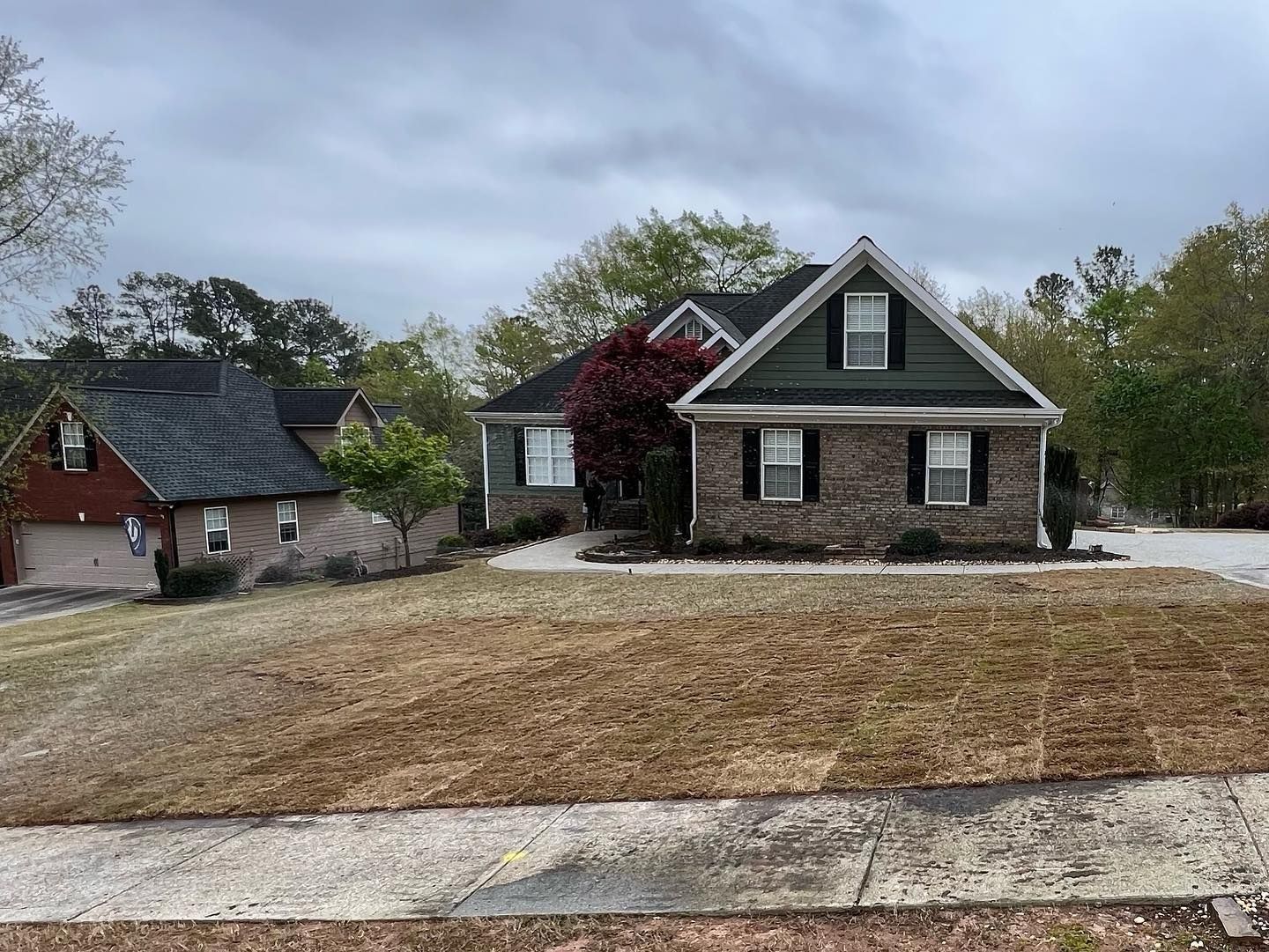 Two brick houses on a slight hill with a brown lawn and cloudy sky.