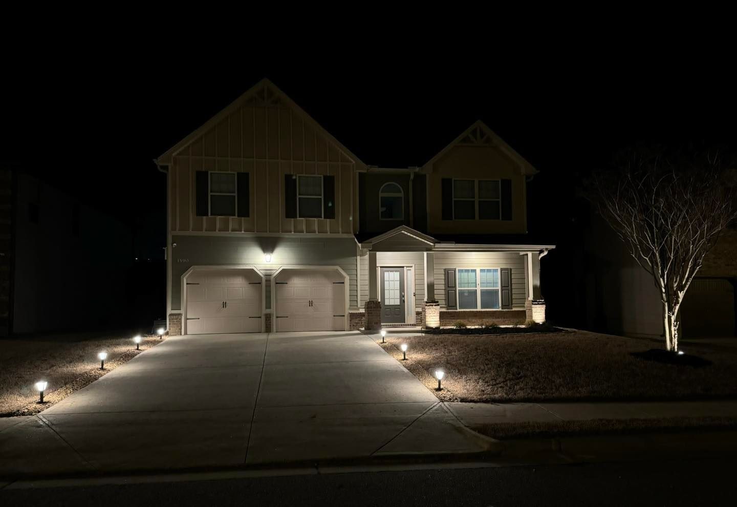 A two-story house illuminated at night with landscape lighting along the driveway and around the front yard.