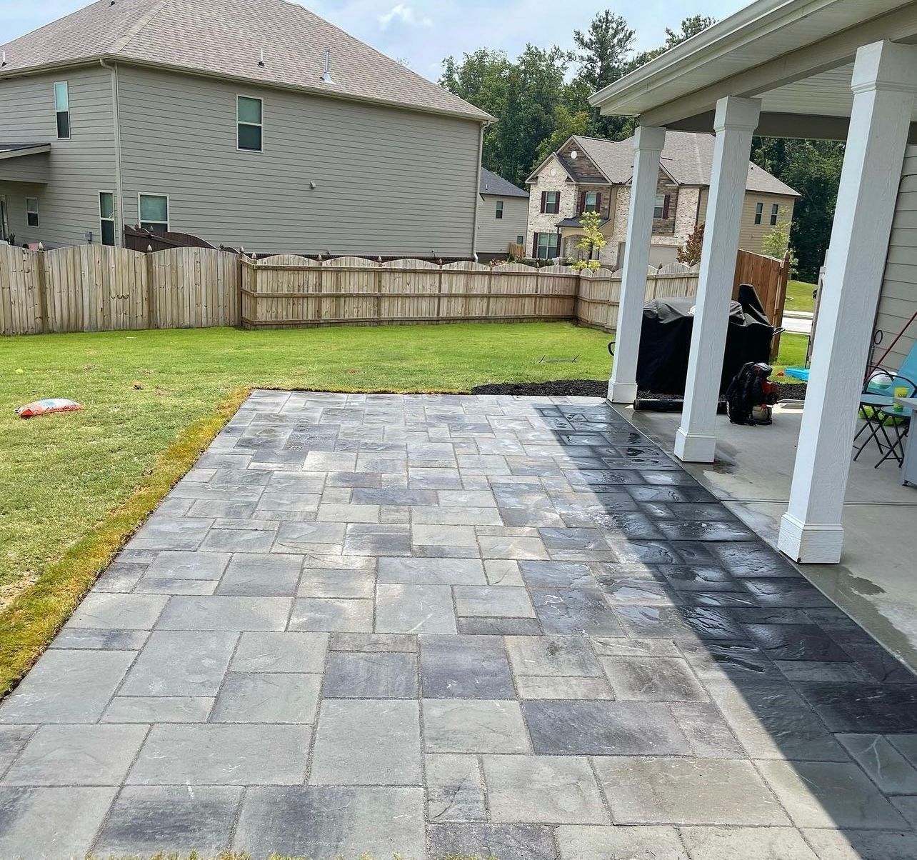 Patio with gray pavers next to green lawn, under a covered porch.