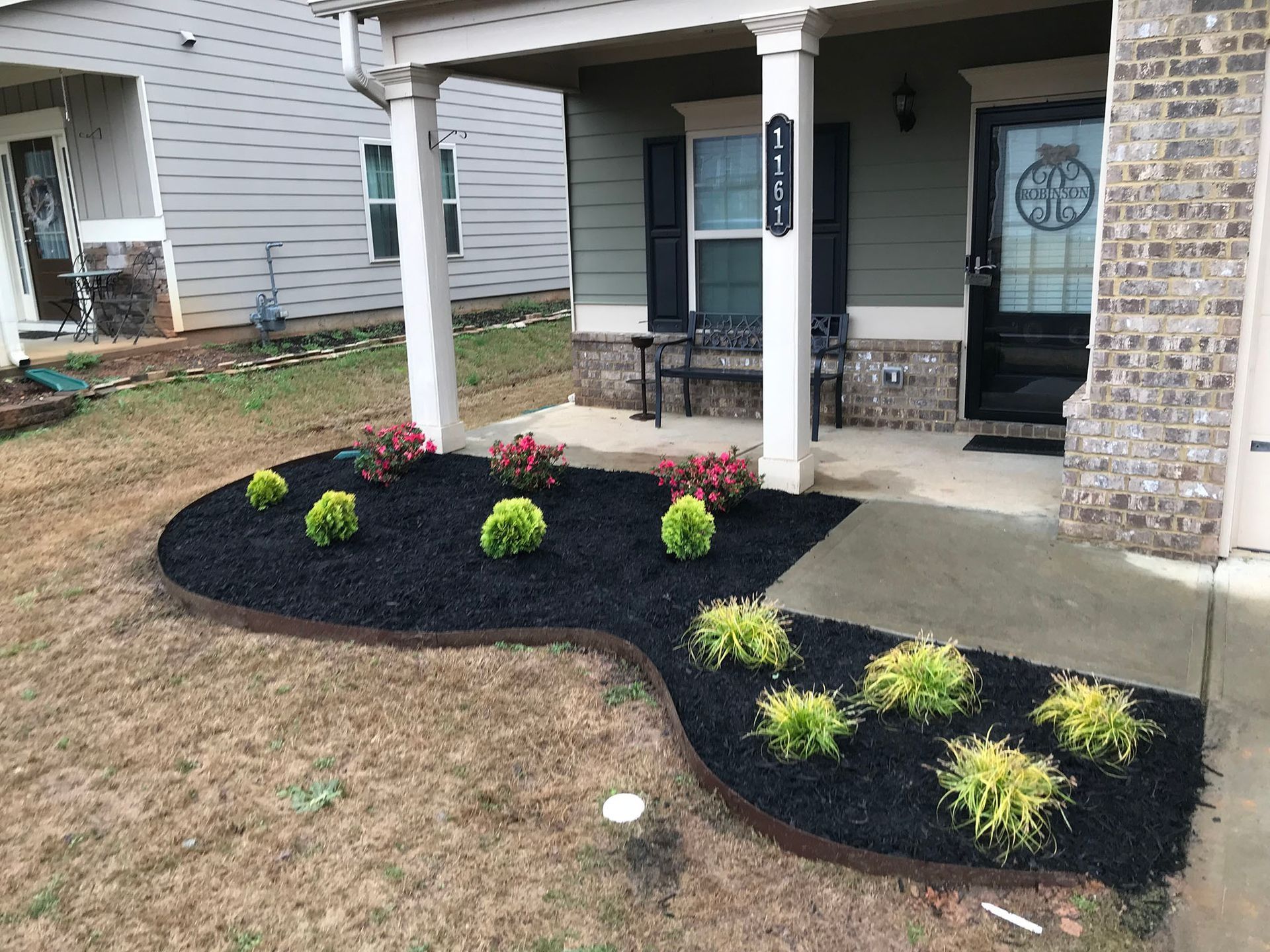 Landscaped front yard with black mulch, flowering plants, and green shrubs in front of a house.