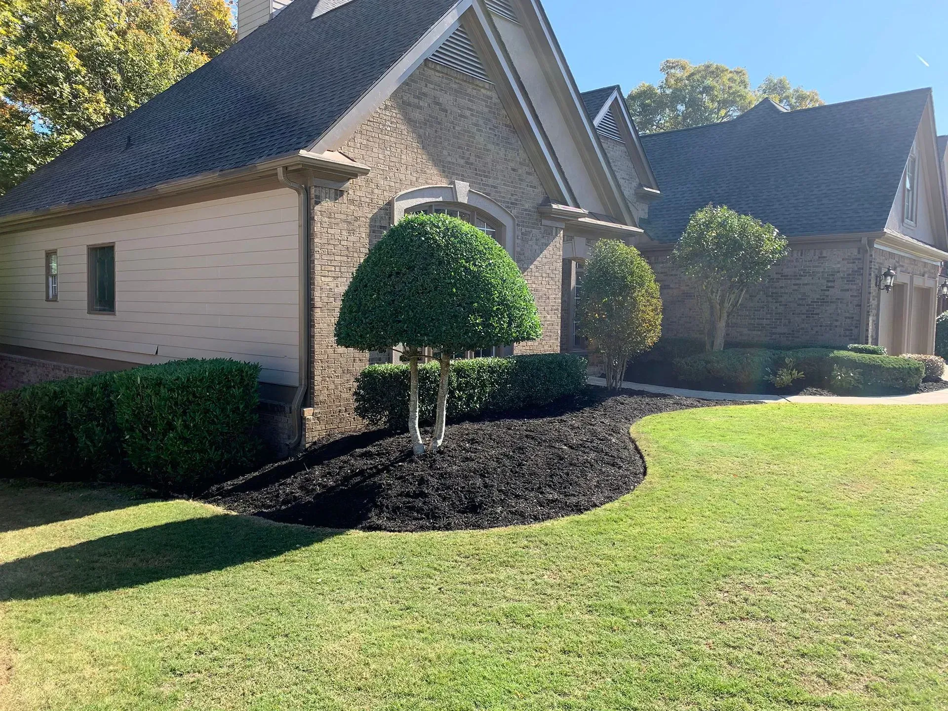 A house with manicured landscaping featuring dark mulch and green grass on a sunny day.