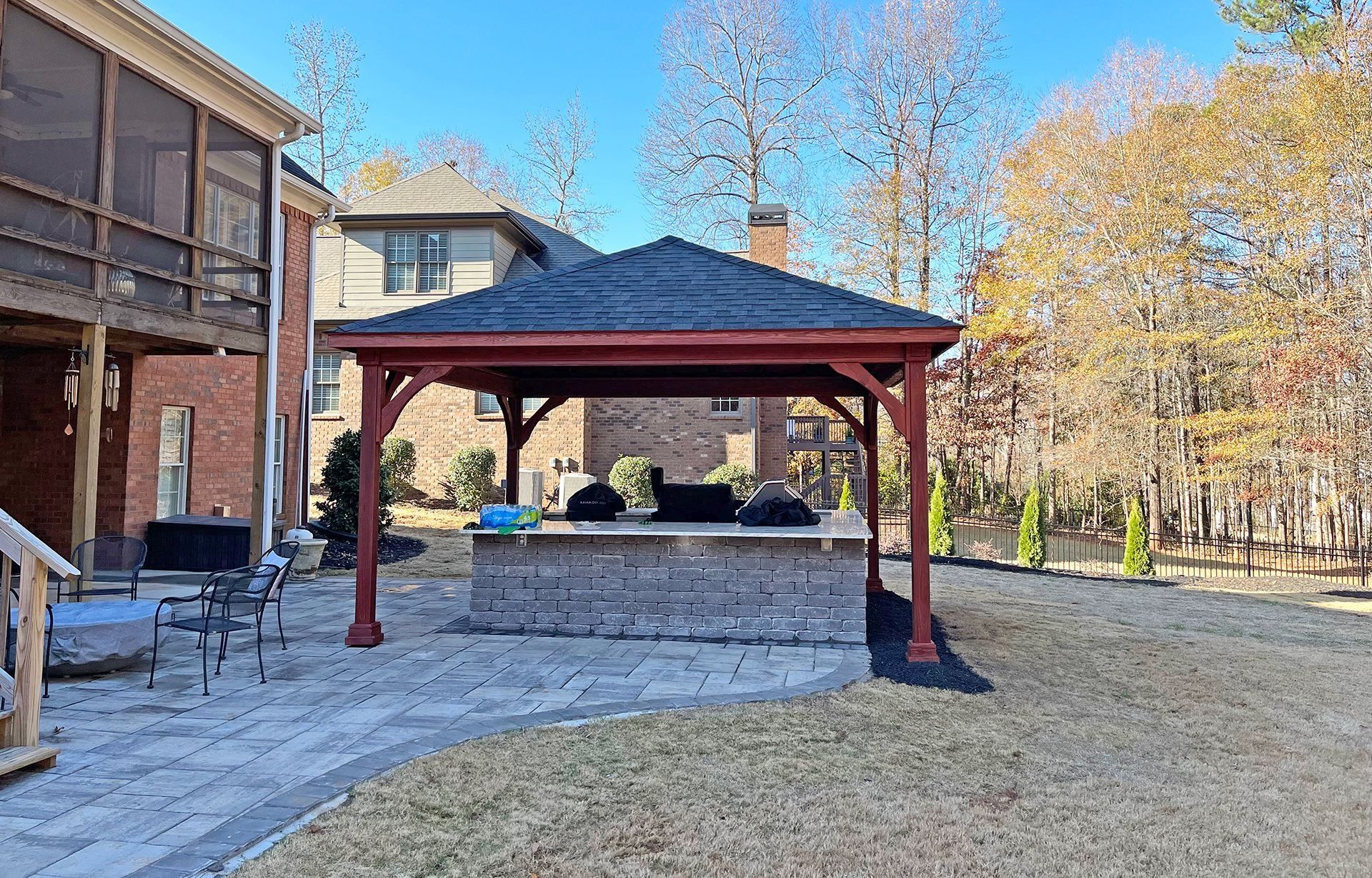 Backyard with a gazebo over a brick outdoor kitchen, next to a home with brick siding and a screened porch.