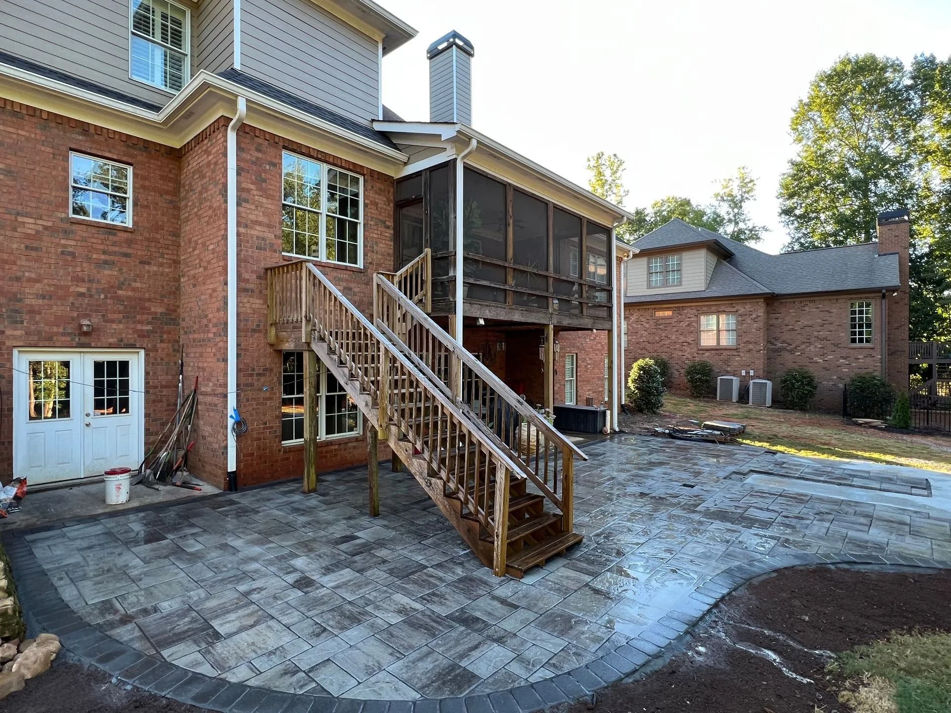 Backyard patio with stairs leading to a screened porch on a brick house. Stone pavers and landscaping.