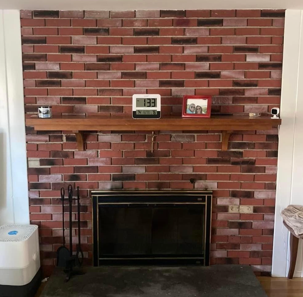 A fireplace with a brick wall and a wooden mantle in a living room