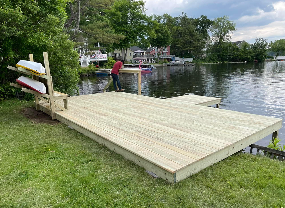 A man is standing on a wooden dock next to a lake