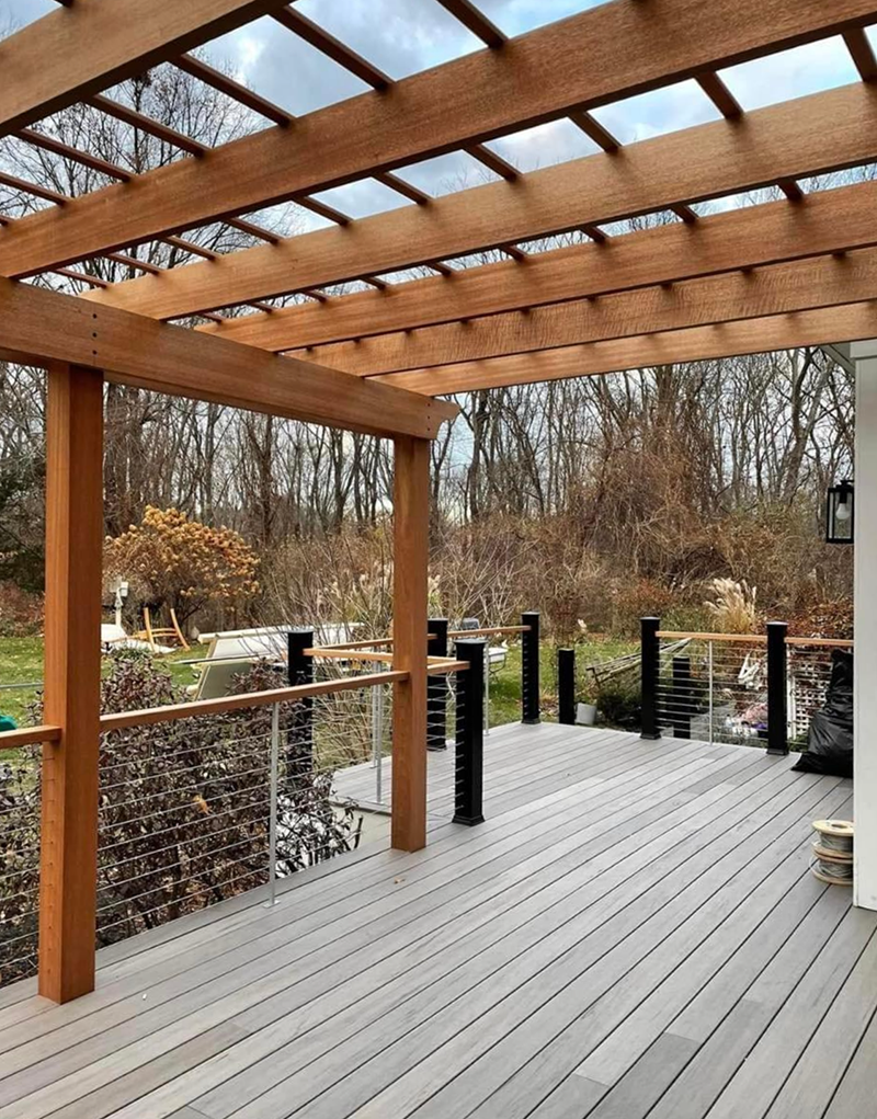 A wooden deck with a pergola and trees in the background