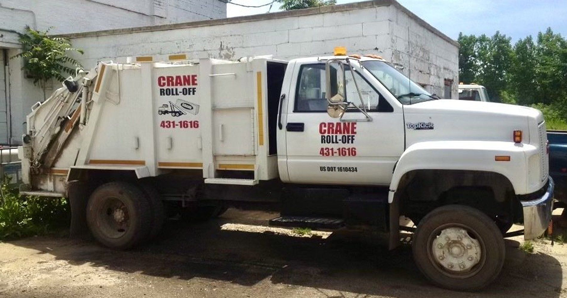 White CRANE utility truck parked beside a building, with a boom and side cargo bed in a yard.