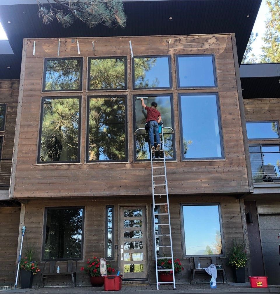 A man on a ladder is cleaning the windows of a house.