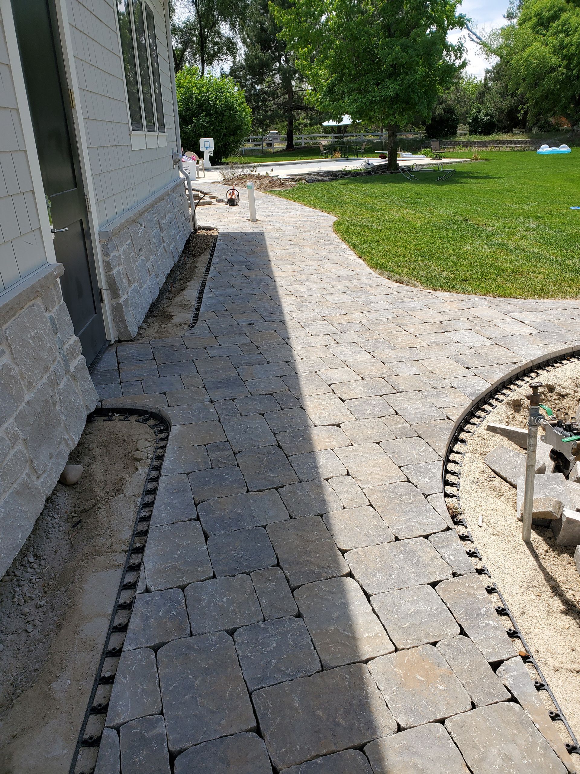 A brick walkway is being built in the backyard of a house.