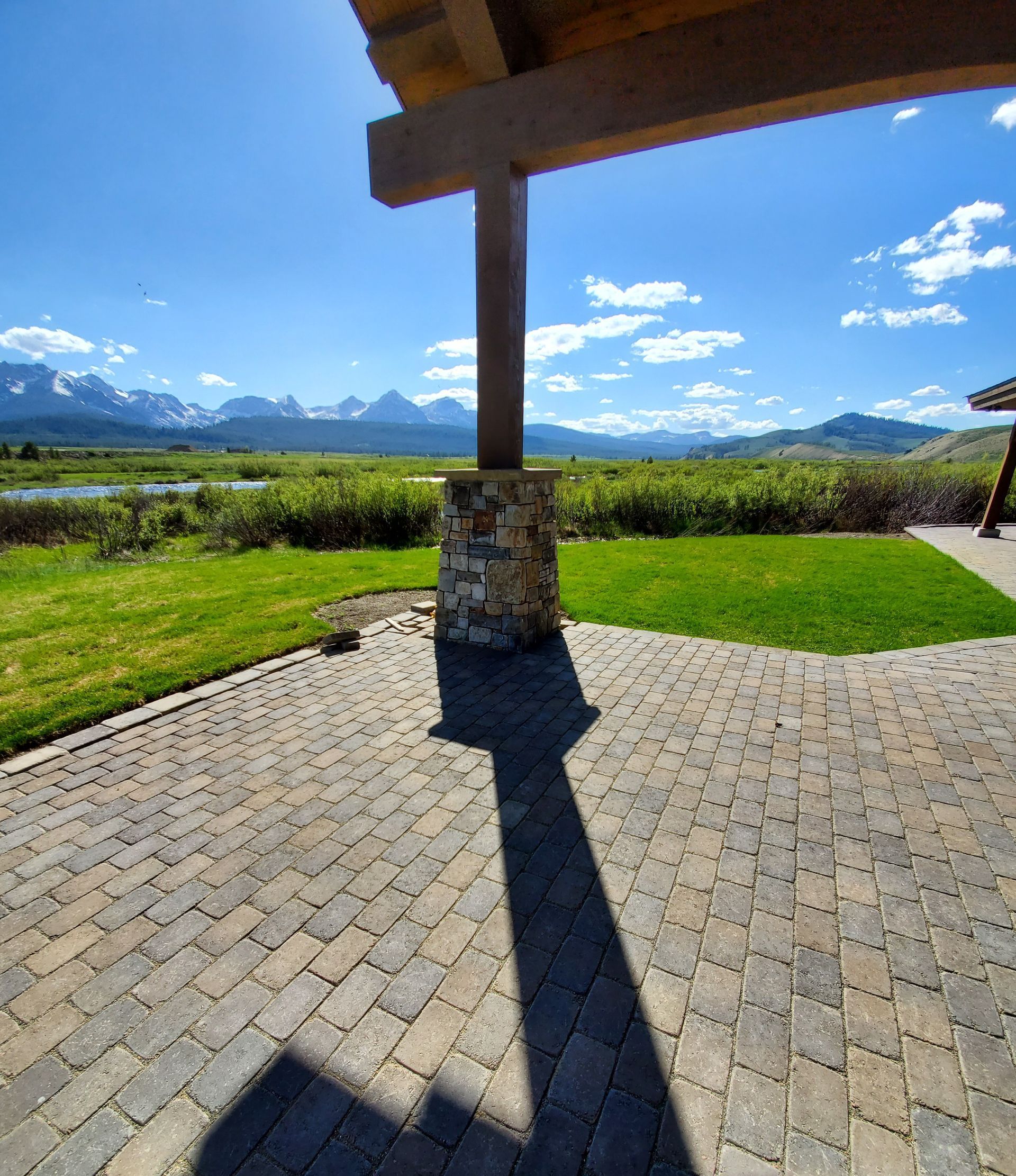 A shadow of a person is cast on a brick patio with mountains in the background.