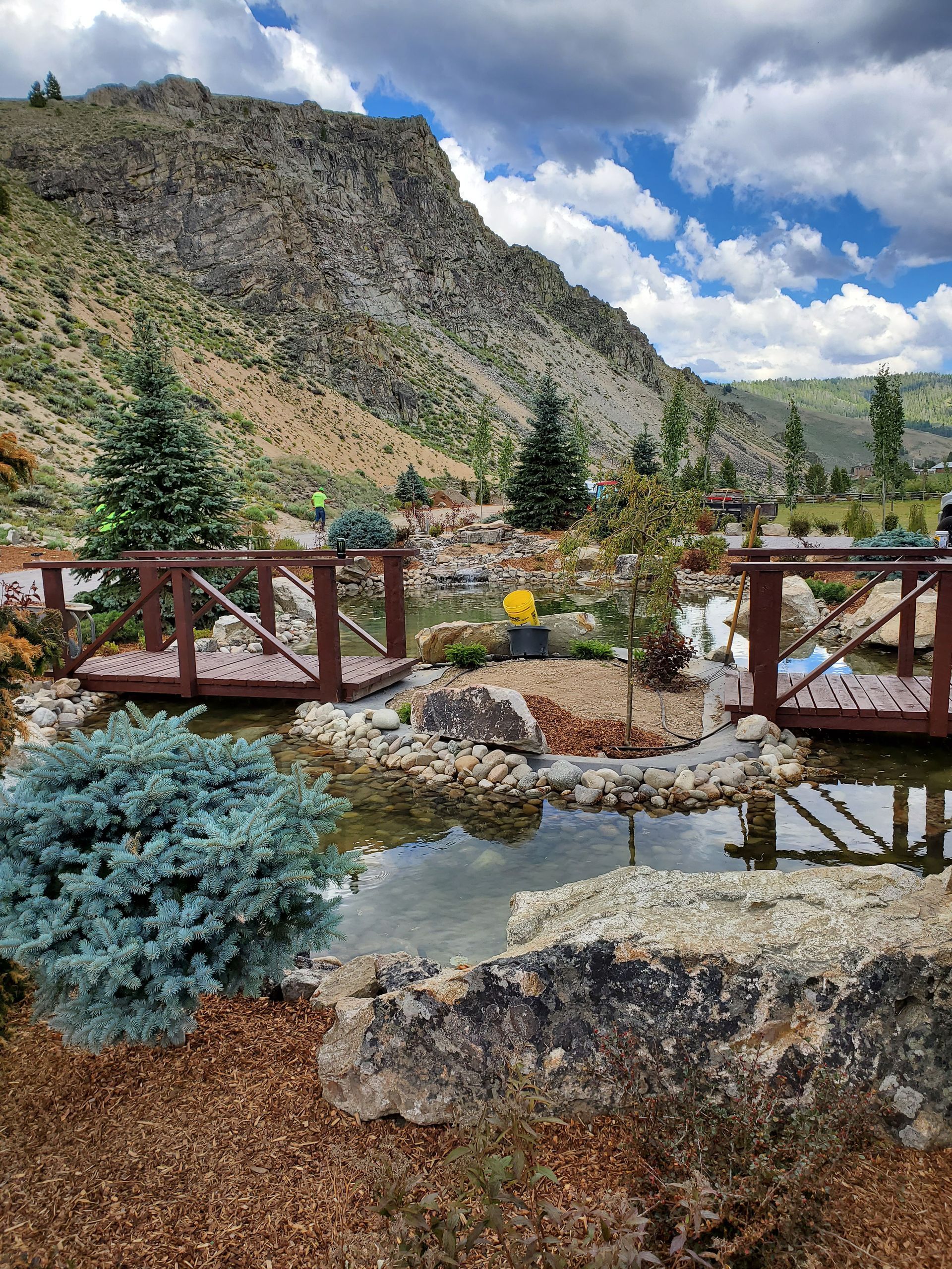 A bridge over a pond in a garden with mountains in the background.
