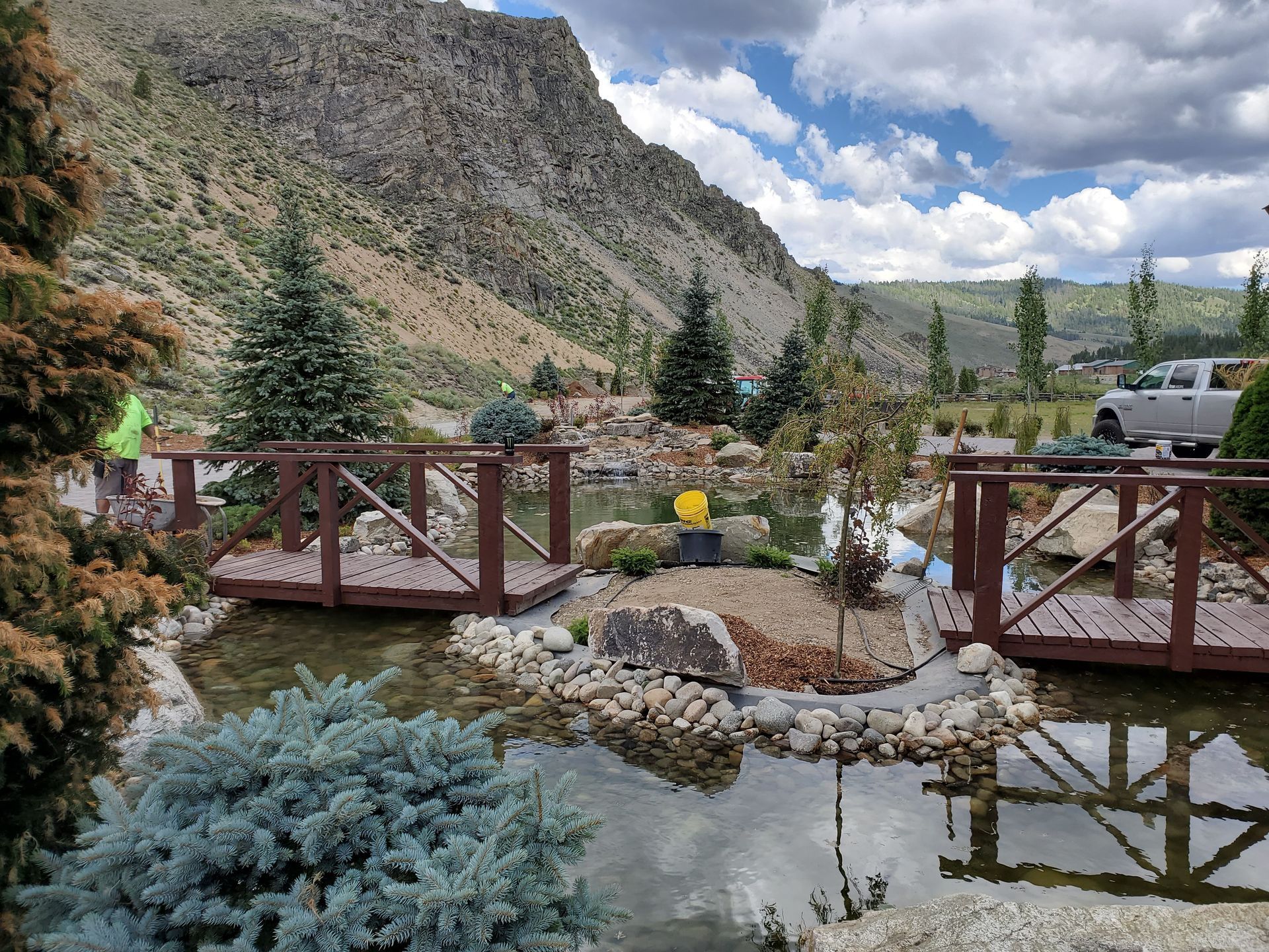 A wooden bridge over a pond with mountains in the background.