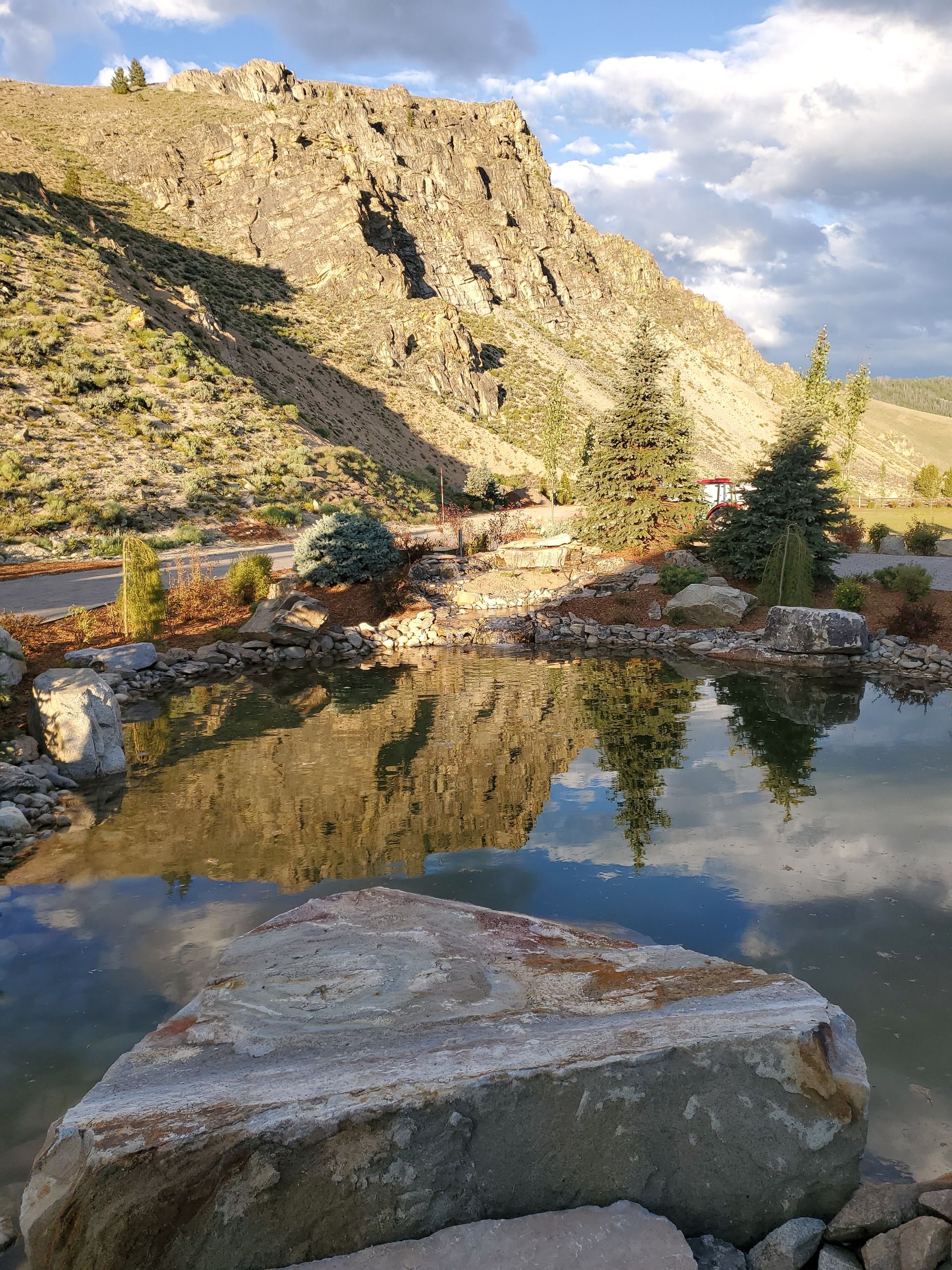A large rock is sitting next to a lake with a mountain in the background.