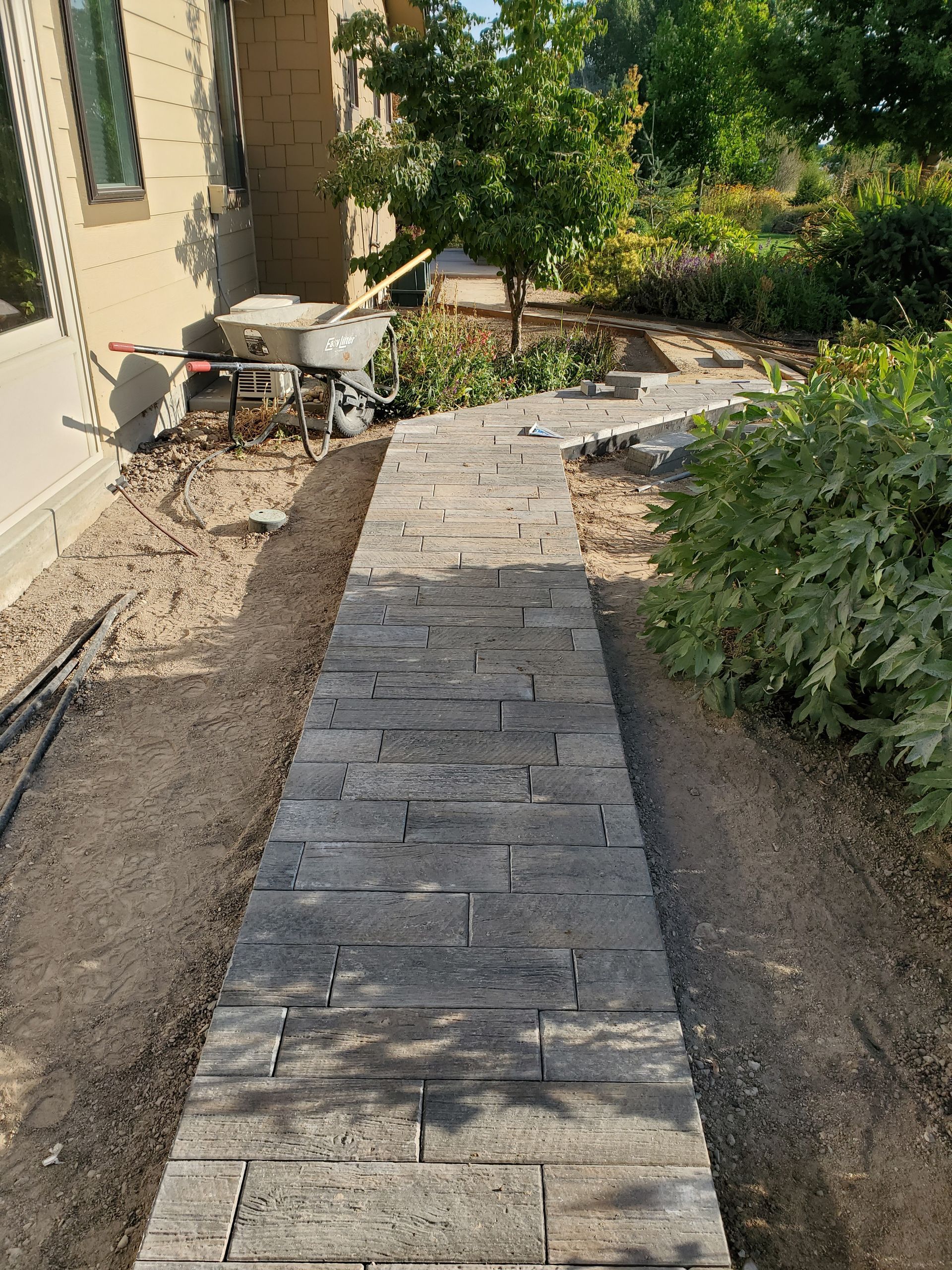 A stone walkway is being built in a garden next to a house.