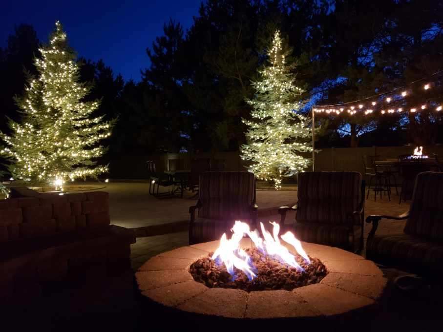 A fire pit surrounded by chairs and christmas trees at night.