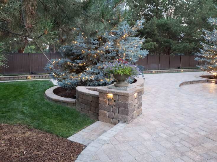 A backyard with a brick walkway and a tree with lights on it.