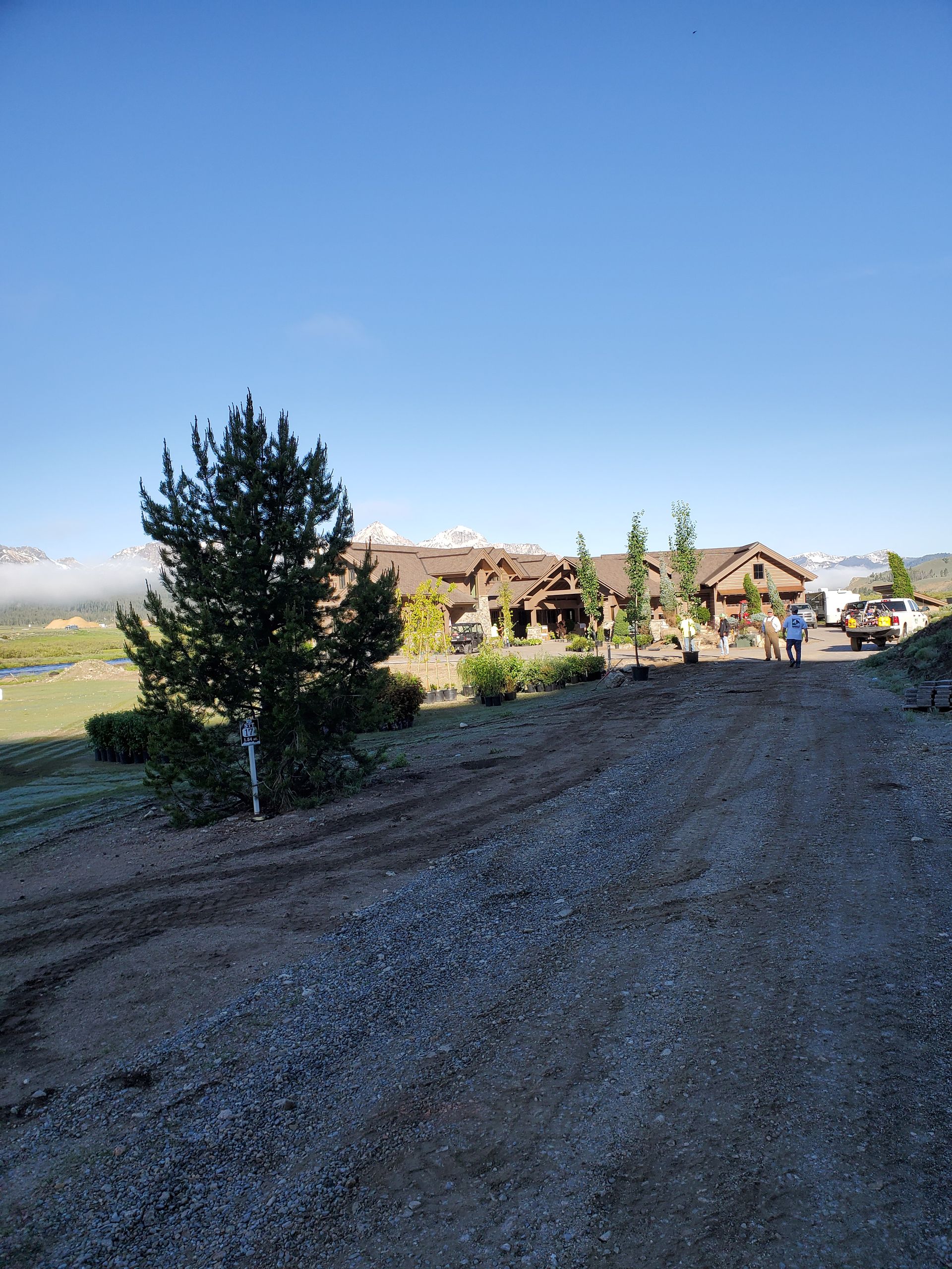 A dirt road leading to a large house with trees on the side of it.