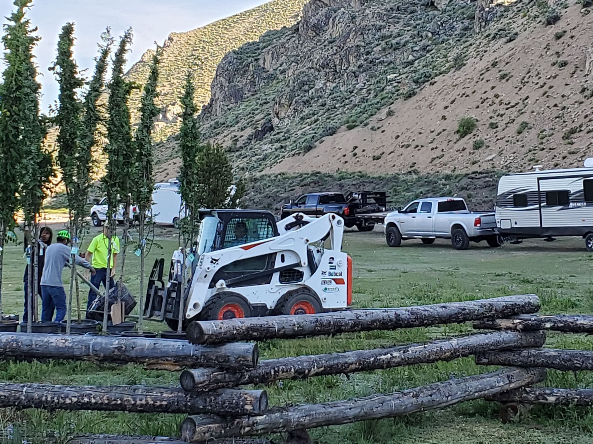A bobcat tractor is parked in a field next to a wooden fence.