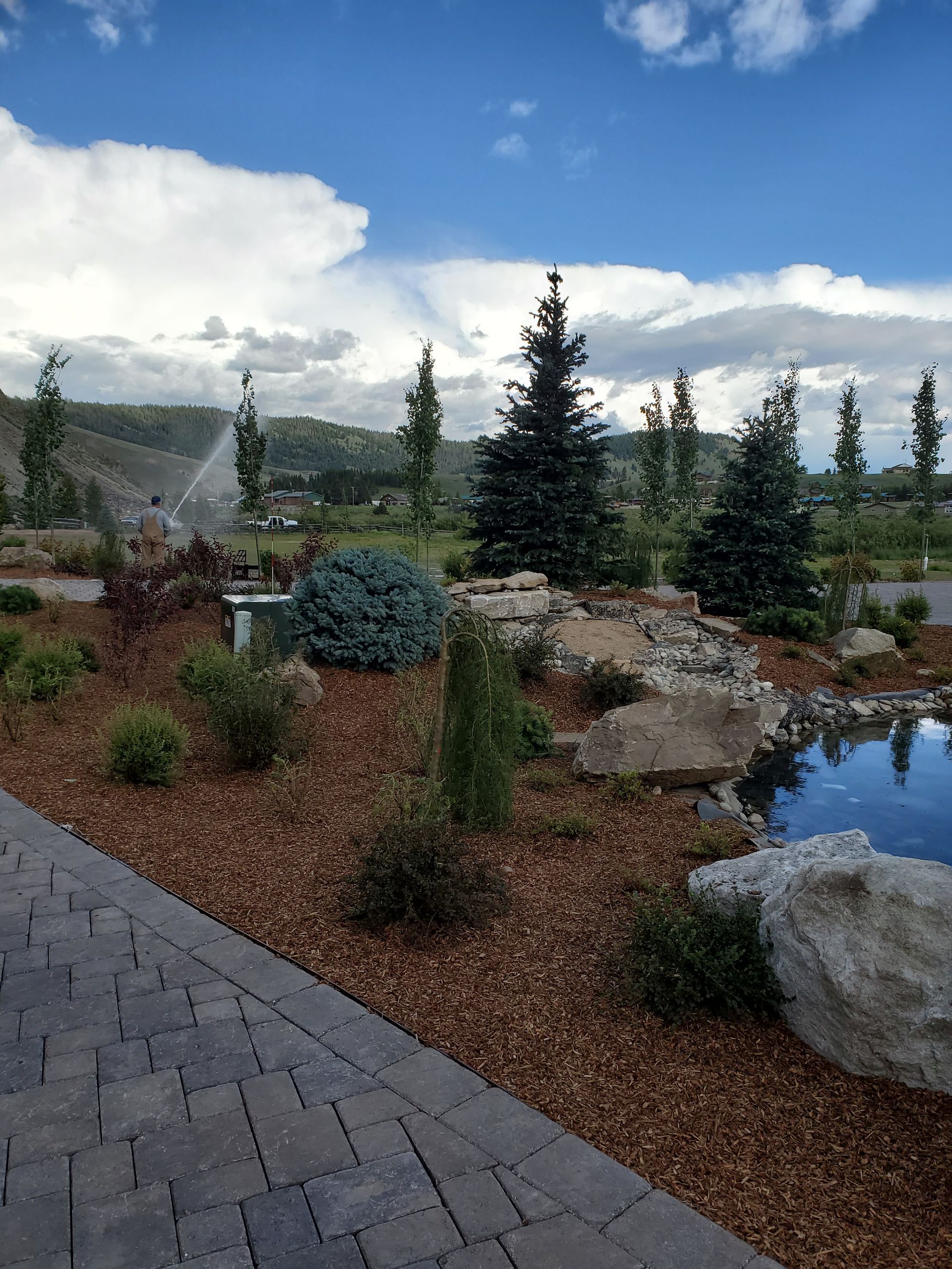 A brick walkway leading to a pond surrounded by trees and rocks